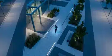 Aerial view of a person walking through a modern city plaza at dusk, holding a glowing tablet, demonstrating navigation through digital trends.